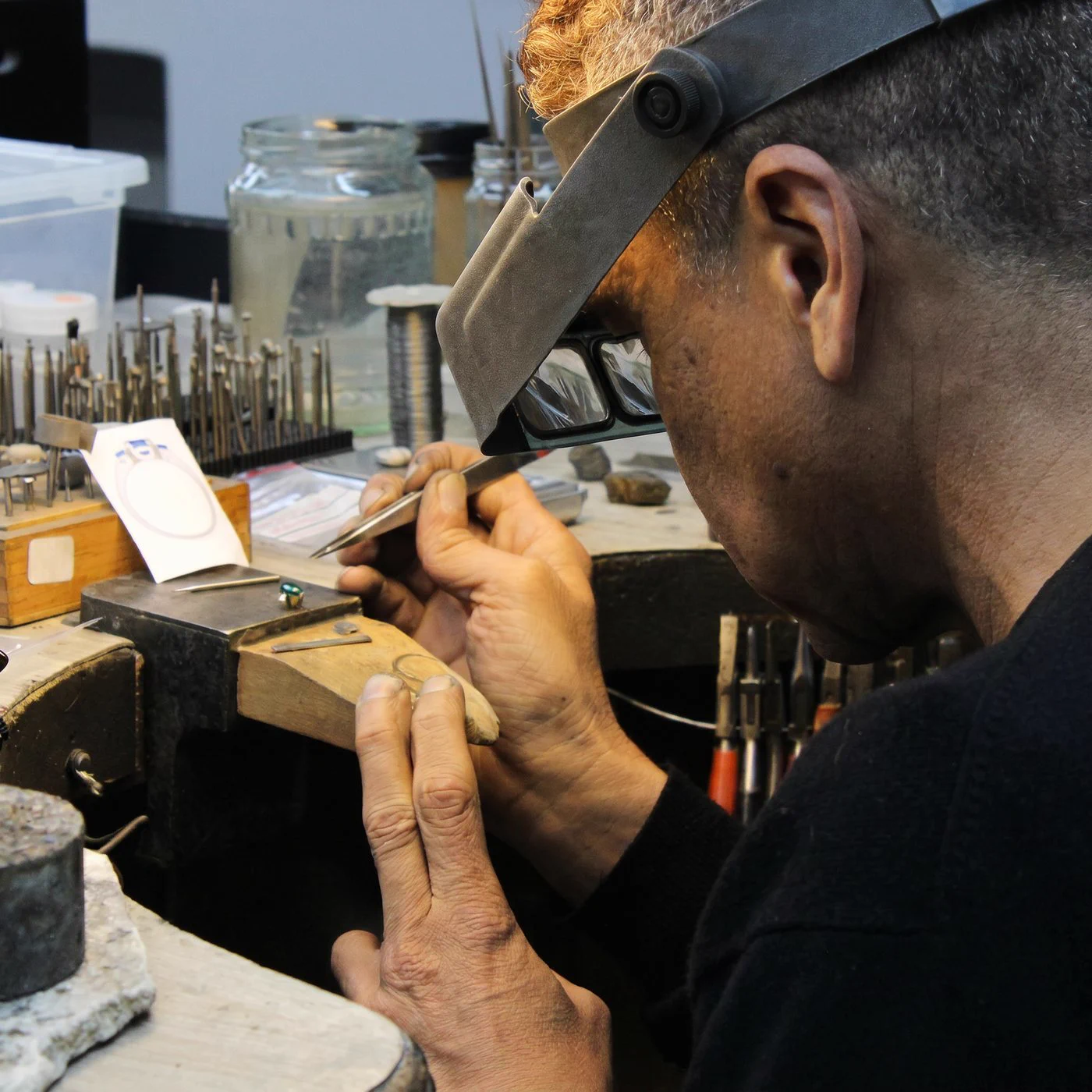 A goldsmith shaping a piece by hand under a magnifier at the bench